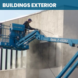 Worker on a lift power washing the side of a commercial building